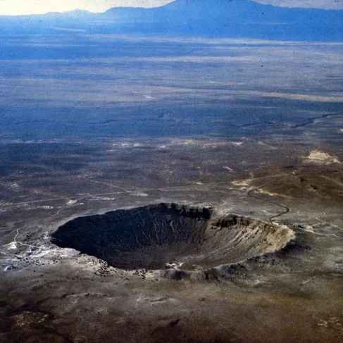 Aerial photograph of Meteor Crater, Arizona: a circular bowl with a raised rim standing in flat desert.
